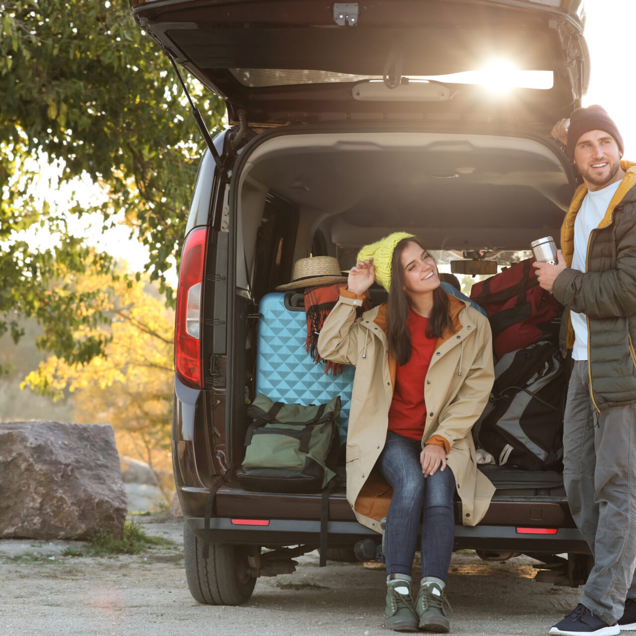 Young couple packing camping equipment into car trunk outdoors Young couple packing camping equipment into car trunk outdoors