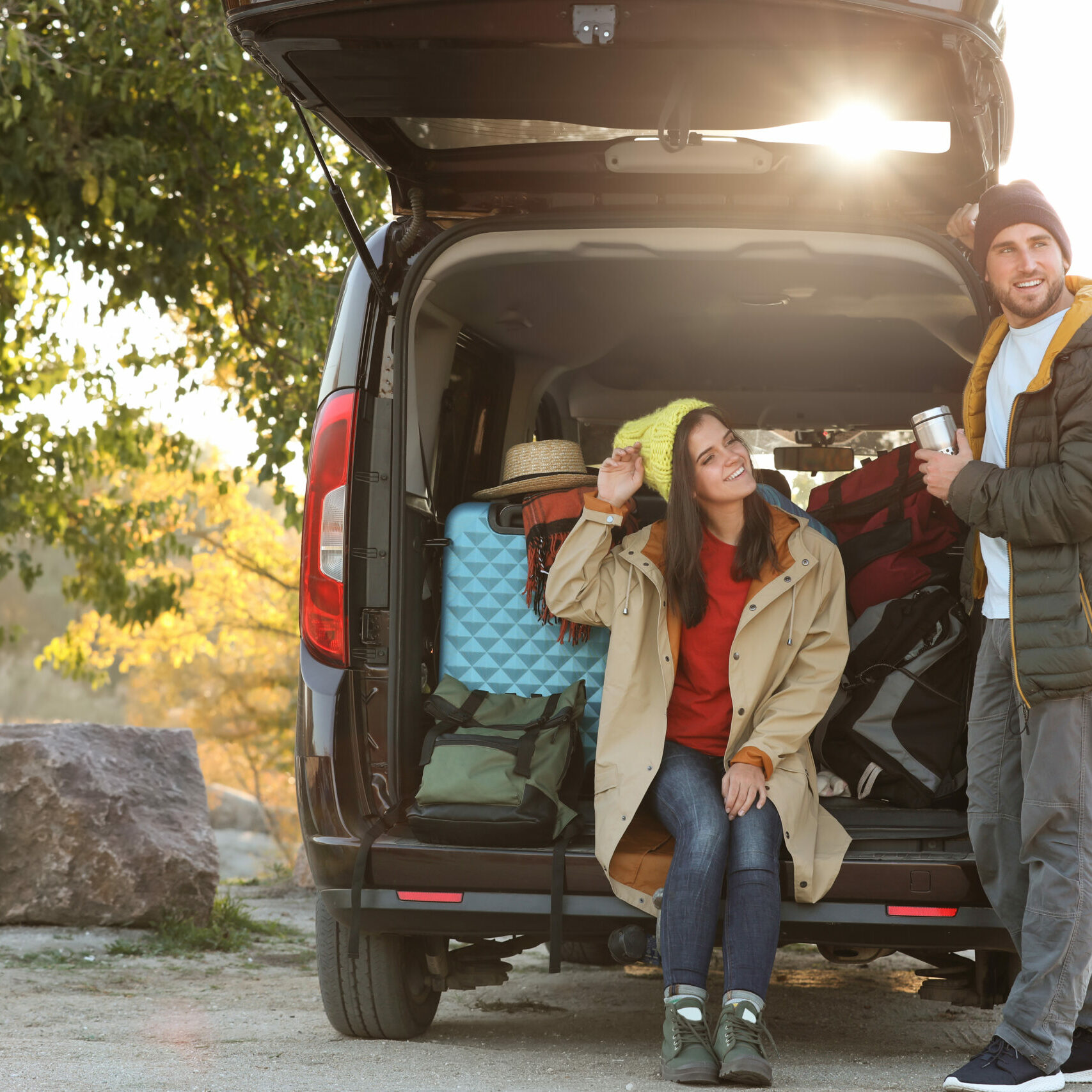 Young couple packing camping equipment into car trunk outdoors